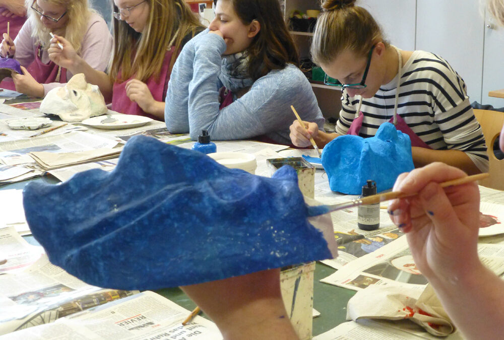 25. Die Masken bekommen ihr endgültiges Gesicht durch die farbige Bemalung. Trotzdem bleiben sie beim Maskenspiel sehr wandelbar. Mit jeder Neigung des Kopfes oder Blickrichtung verändert sich ihr Ausdruck.