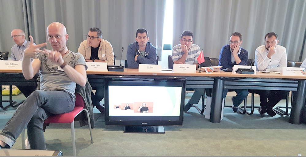 RWB Essen – Spreadthesign in Rennes – Besprechungen im Konferenzraum der Universität Rennes –  Im Vordergrund: Dolmetscher David Niemann, im Hintergrund: Alan Robinson, Schulleiter des Doncaster Special Communication Colleges (ganz rechts), daneben das türkische Team Spreadthesign: Soner Ogul, Ali Özer, Ahmet Yigit, Emin Gümüsel und Hasan Büyükkömürücü.